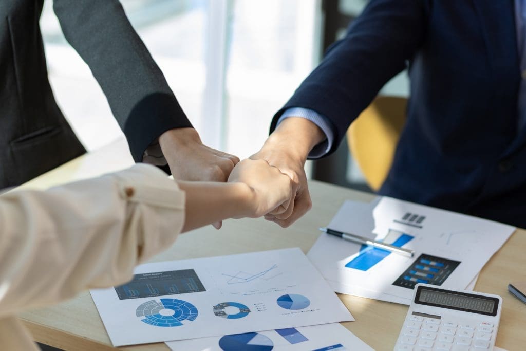 Represents a Partnership Agreement as three people fist bumping over business diagrams.